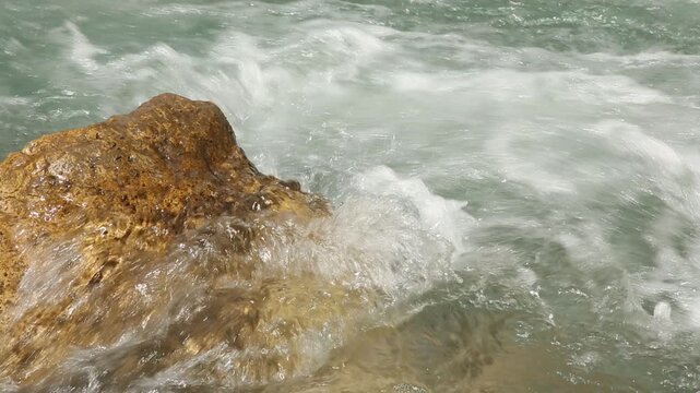 Ocean surf action. White froth collides with jagged cliffs beneath bright sunlight. Sea waves collide with exposed rocks creating spray and foam in sunlight context