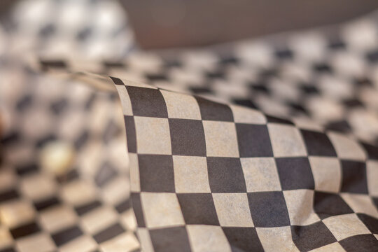 Black and white checkered paper covers food items. Paper wraps food, creating a checkered pattern. Folds and creases show soft, flexible texture. Grainy surface highlights material's natural feel
