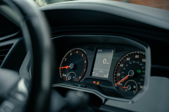 A close-up photo of a car dashboard showing the speedometer, tachometer, and digital display screen. The speed is at 0 km/h, and the screen also shows the time, temperature, and trip information.