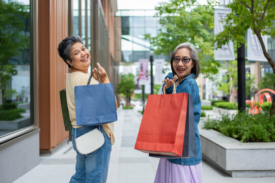 Portrait of Two Asian senior women standing outdoors with shopping bags. 