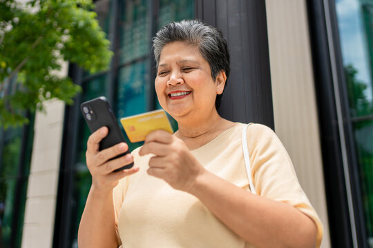 Asian senior woman using phone shopping online outdoors in the city. 