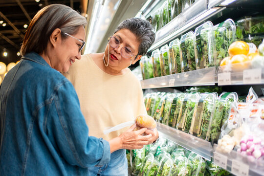 Two cheerful Asian senior women shopping for groceries in a supermarket. 