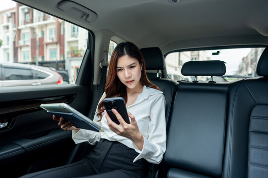Professional Asian woman using phone while sitting in back seat of a car.