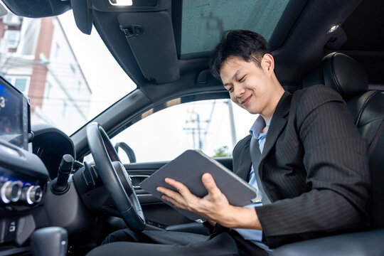 Asian businessman using digital tablet, working inside a car while driving. 
