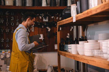 Fototapeta premium Retail store clerk examining shelf inventory in rustic shop interior with ceramic bowl display and bottled goods