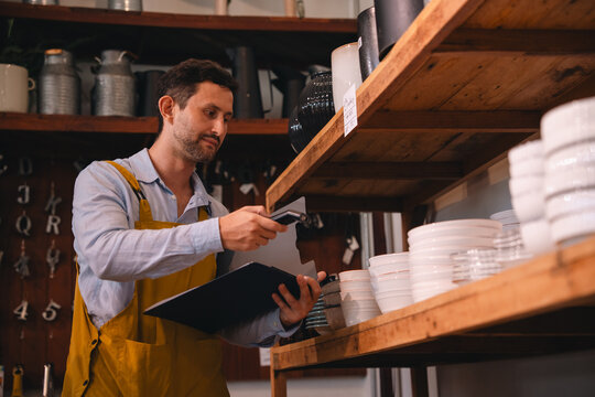 Retail worker scanning ceramic bowl in store aisle, inventory check in kitchenware shop with focused male clerk