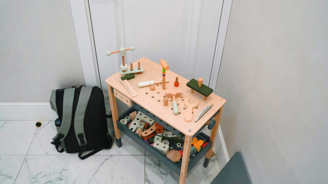 Wooden toy workbench with tools and parts in a room with tiled floor