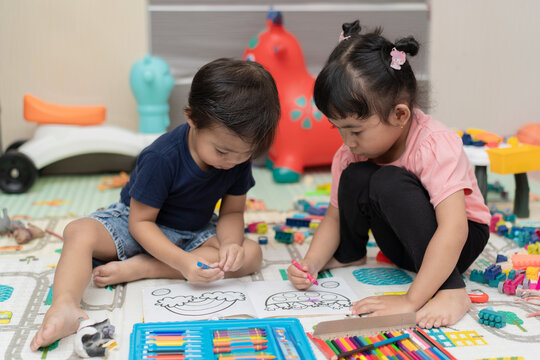 Two young children sitting on floor coloring book with crayons