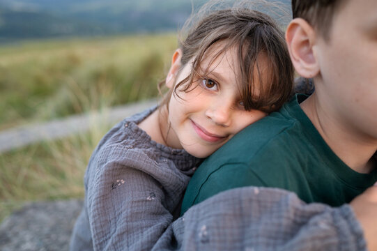 Girl resting head on brother shoulder smiling in soft evening light