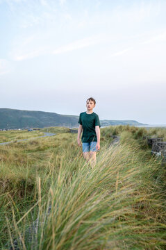 Boy walking through tall grass in coastal landscape outdoors