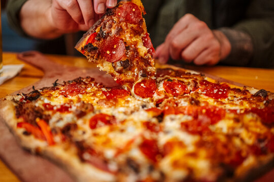 Hand lifting slice of pizza with melted cheese in restaurant.