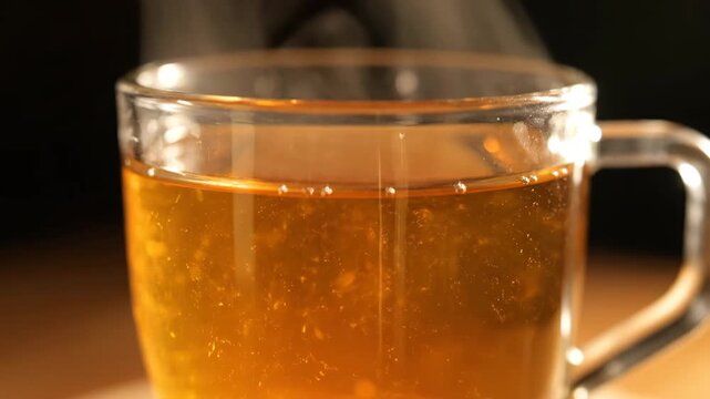 Macro shot of hot amber tea or herbal infusion steaming in a clear glass mug. cozy warm beverage showing health benefits and comfort against a dark background.
