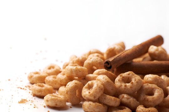Side profile of cereal ring pieces with cinnamon sticks and dust, isolated on white background with bright cinematic lighting