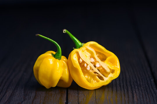 Yellow habanero peppers with sliced half on wooden surface. Fresh chili pods interior detail rustic composition