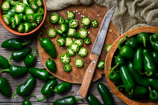 Top view of jalapeno peppers with slices and bowl on wooden board. Fresh green chili cooking preparation natural surface