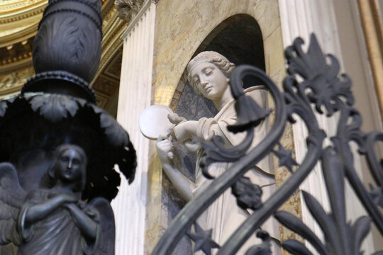 Dettaglio artistico di una statua di angelo in marmo bianco dietro una cancellata in ferro battuto decorata, architettura barocca e scultura sacra all'interno di una chiesa storica.
