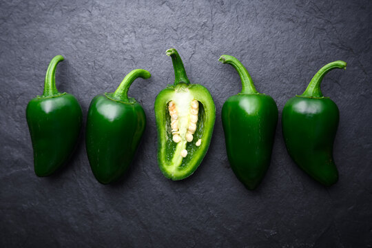 Jalapeno peppers with one cut open piece revealing seeds on dark background. Spicy vegetable composition with dramatic lighting