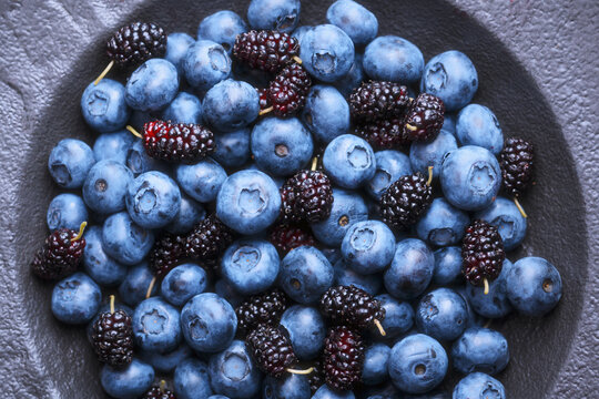 Close up view of blueberries and mulberries filling the black plate. Fresh blue berries texture, antioxidant superfood concept. Top view