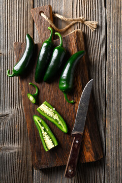 Black jalapeno with knife on rustic wooden cutting board close up. Green mexican jalapeno hot peppers