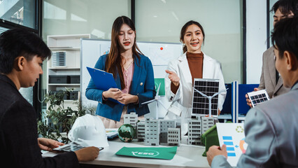 Business team meeting with engineers discussing renewable energy project using solar panel and wind turbine models in modern office, presenting green city planning concept © NanSan