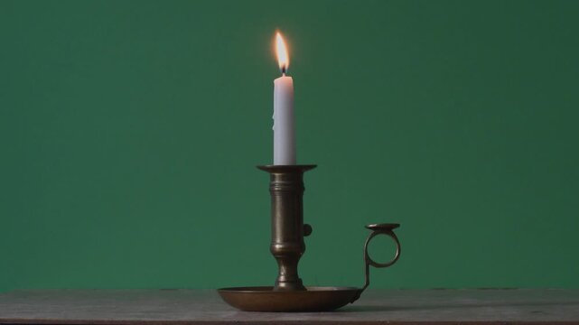 A man in red places a burning white candle in an antique candlestick on the table - Green background