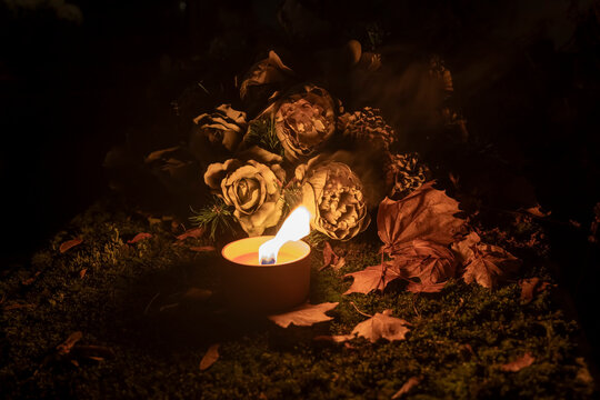 Glowing candle and flower bouquet on an autumn grave at night