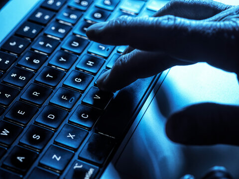 Hacker typing on backlit laptop keyboard depicting cybercrime