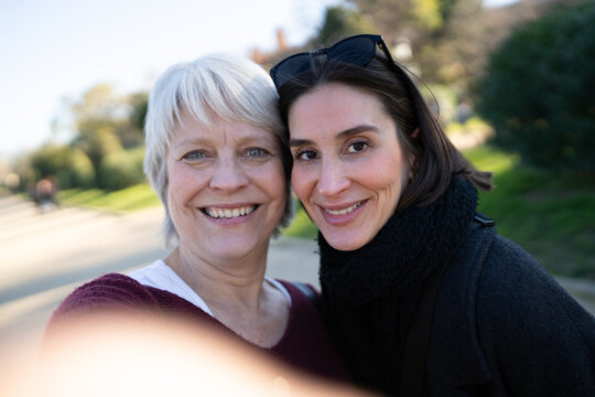 Group of female friends smiling and posing for a selfie together in a beautiful park on a sunny day