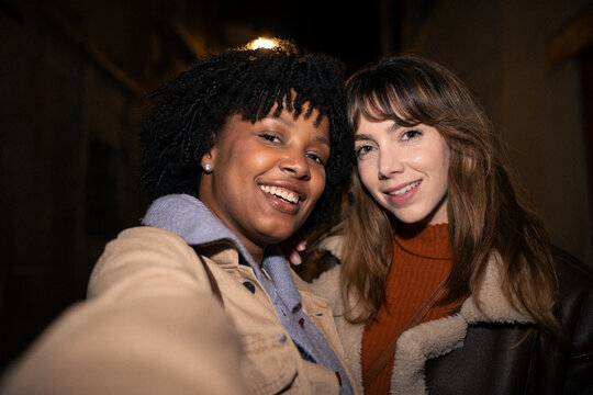 Happy friends in winter jackets taking a selfie outdoors at night