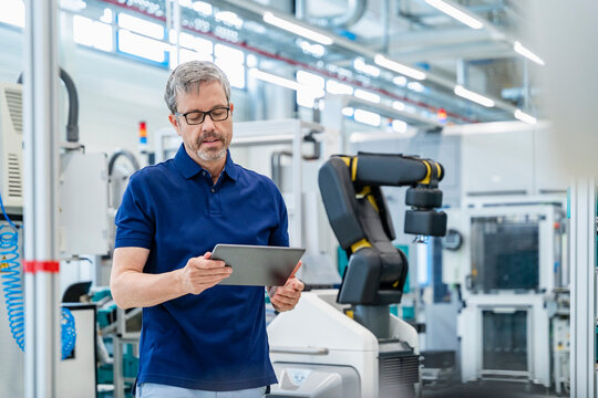 Engineer using tablet in automated factory with industrial robot