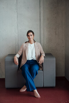 Smiling businesswoman with crossed legs sitting on armchair at office