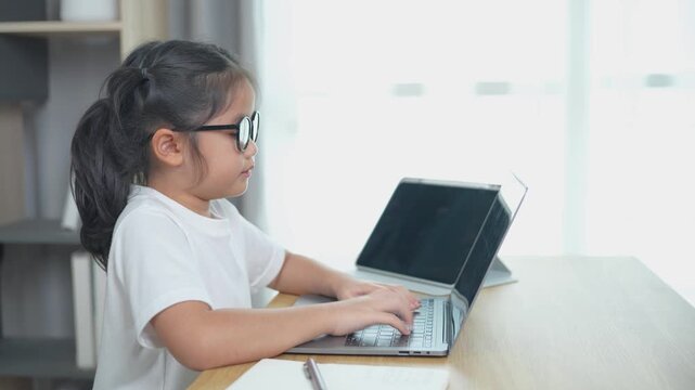 Young girl with sunglasses typing on laptop at home, focused on work, modern workspace, bright room, learning, childhood productivity, technology usage