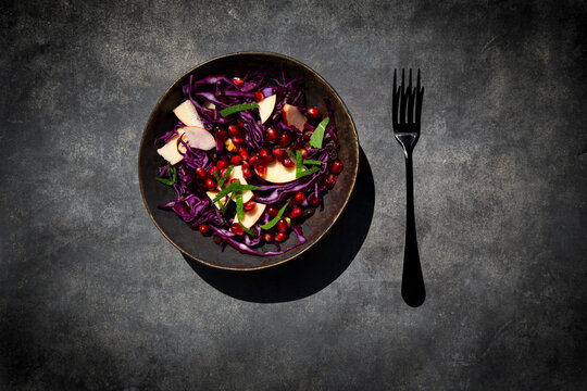 Red cabbage, apple and pomegranate salad on dark concrete