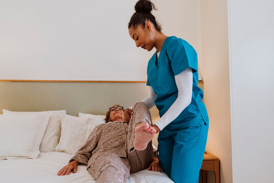Caregiver assisting senior woman with leg movement on bed at home