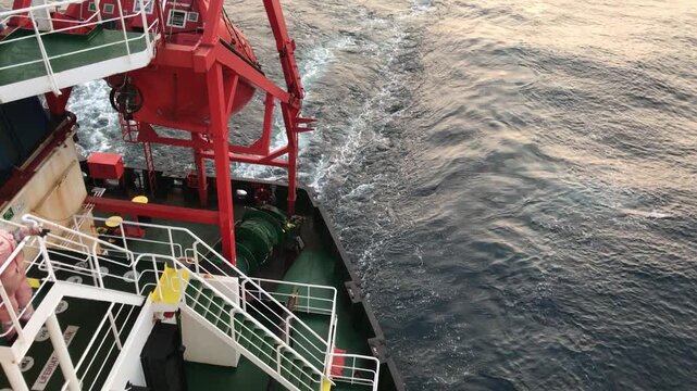 View of the lifeboat and propeller wash of a merchant ship underway at sea in the evening