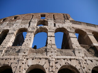 Obraz premium Colosseum facade with arches under blue sky, Rome landmark