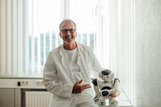 Smiling doctor in a lab coat presenting a robot in a hospital