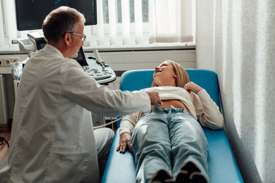 Doctor performing ultrasound on smiling pregnant patient in clinic