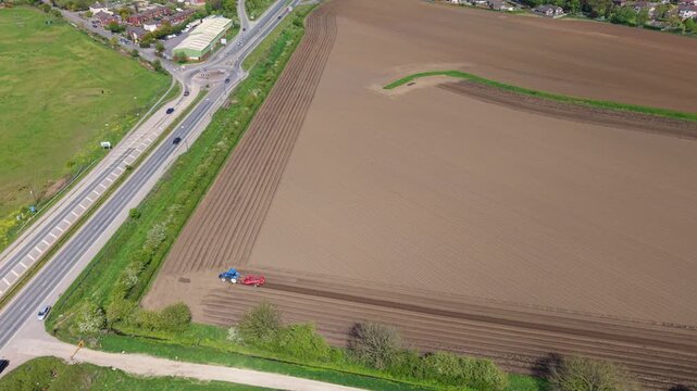 Aerial top down view of a tractor ploughing fields and creating geometric soil furrows near Ferrybridge Yorkshire UK