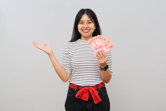 A woman receives a lot of rupiah banknotes, isolated on a white background with a surprised facial expression, opening her hands behind her back in empty space, presenting or showing something.