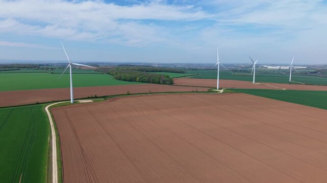 High angle aerial drone view of a large wind turbine array in brown and green patched rural fields in the United Kingdom
