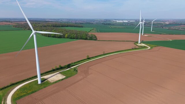 High angle aerial drone view of a large wind turbine array in brown and green patched rural fields in the United Kingdom