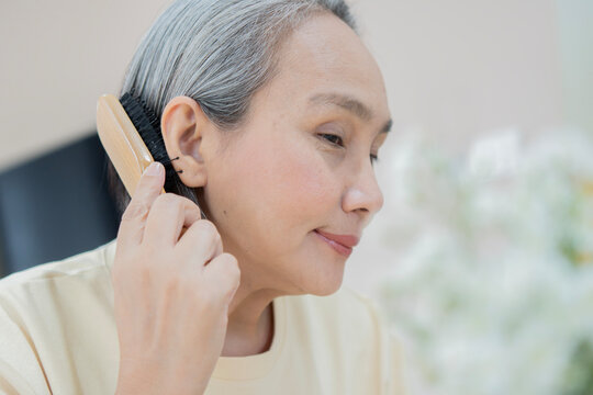 Asian mature woman combing her gray hair at home. Care senior hair hygiene