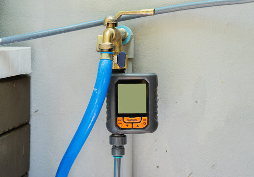 Photo of a gray digital water timer with faucet setting on wall at home.