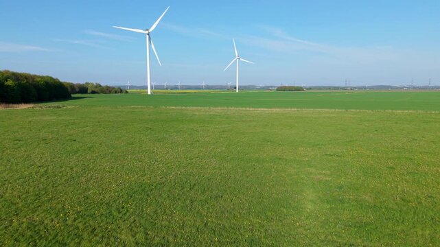 Aerial perspective of clean energy wind turbines operating amidst colorful agricultural land and rural pastures in Great Britain
