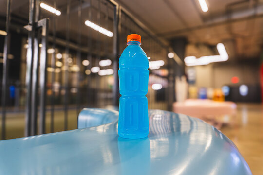 Blue Isotonic Sports Drink in Unlabeled Plastic Bottle with Orange Cap on Blue Surface in Modern Urban Fitness Center