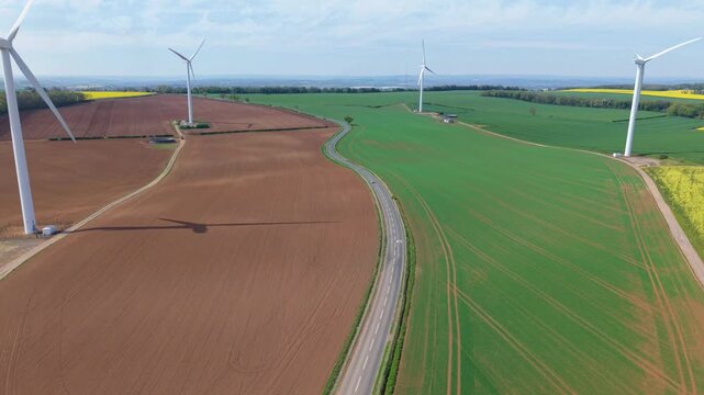 High angle aerial drone view of a large wind turbine array in brown and green patched rural fields in the United Kingdom