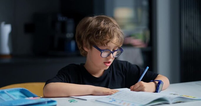 Male Student Wearing Glasses Intensely Engaged In Studying His Workbook At Kitchen Table In Evening