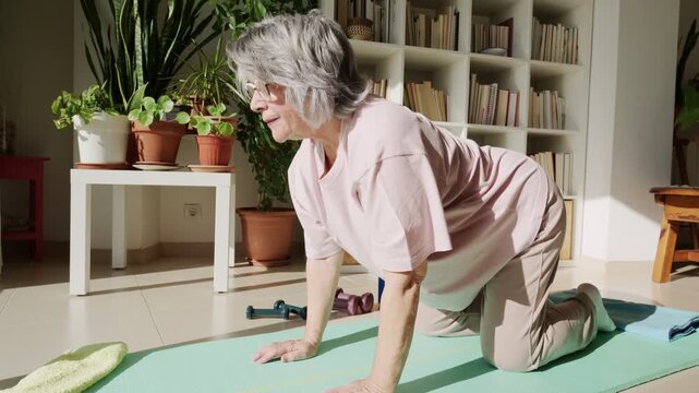 Elderly woman doing cat-cow yoga pose for back health at home