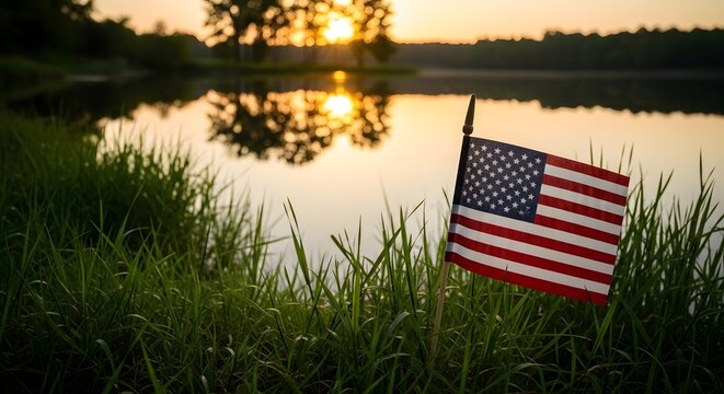 Small american flag planted in grass by a lake at sunset
